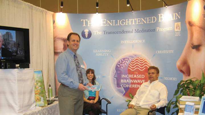 020-booth.jpg - Dr Michael Beresford, experienced in EEG research, stands in the booth at a Yoga Conference attended by 6,000 participants. During their presentation at the conference, they had about 700 conversations with interested viewers at the booth plus continuous presentations through the conference days.