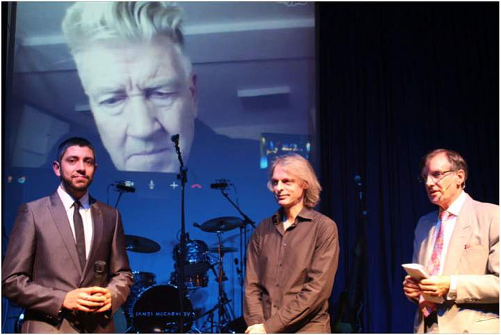 16.jpg - Dr Peter Warburton, right, Chairman of Maharishi Foundation UK, introduces two military veterans at the benefit dinner while Dr David Lynch (above) listens on the videoconference link.