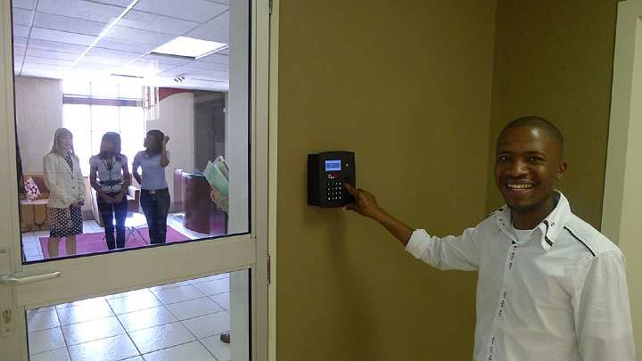 SouthAfrica099.jpg - A student at the Maharishi Institute demonstrated the modern electronic, digital fingerprint recognition system used to sign in and out. Inside is Annie Blecher (left) with two MI students.